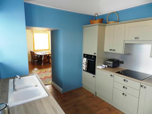 a kitchen with white cabinets and a blue wall at Castleside Croft in Kildonan