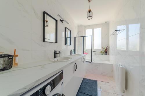 La salle de bains blanche est pourvue de 2 lavabos et d'une baignoire. dans l'établissement Cosy Modern Apartment - 1 minute walk from train station, à Creil