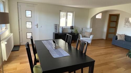 a dining room and living room with a black table and chairs at Appartement spacieux proche de Morges et Lausanne in Aclens