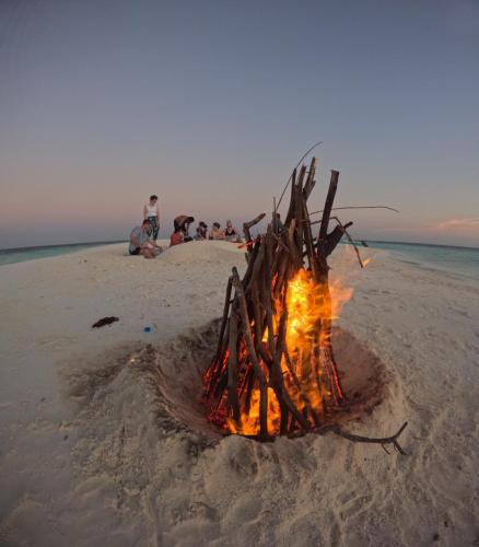 a fire pit on a beach with people sitting around it at Aqua Sunset in Gulhi