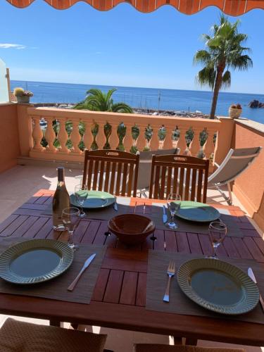 a wooden table with plates and wine glasses on a balcony at Plage de Miramar in Théoule-sur-Mer