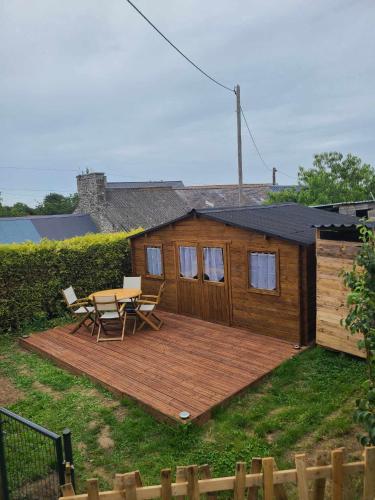 une terrasse en bois avec une table et des chaises devant une cabine dans l'établissement Chambre dans chalet entre terre et mer, à Saint-Lormel