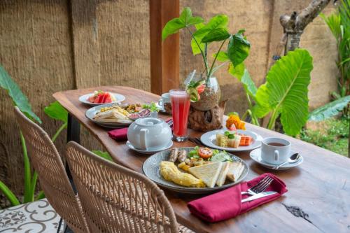 Una mesa de madera con platos de comida encima. en Tiare Villa Ubud by Dhananjaya Hospitality, en Tampaksiring