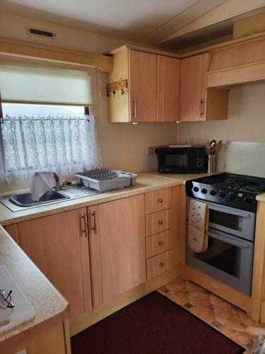 a kitchen with wooden cabinets and a stove and a sink at Kerrys Place, 75 Sealands Caravan Site, Ingoldmells 6 Berth in Ingoldmells