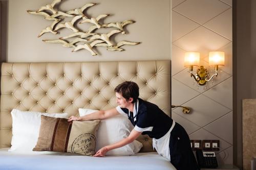 a man putting pillows on a bed in a hotel room at Grand Hotel Des Sablettes Plage, Curio Collection By Hilton in La Seyne-sur-Mer
