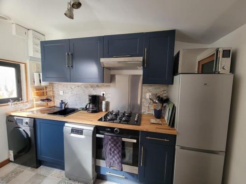 La cuisine est équipée de placards bleus et d'un réfrigérateur blanc. dans l'établissement Maison proche de Honfleur, côte fleurie, à Conteville