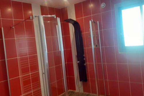 une douche dans une salle de bain aux murs carrelés de rouge dans l'établissement Maison familiale au Hézo, à Le Hézo