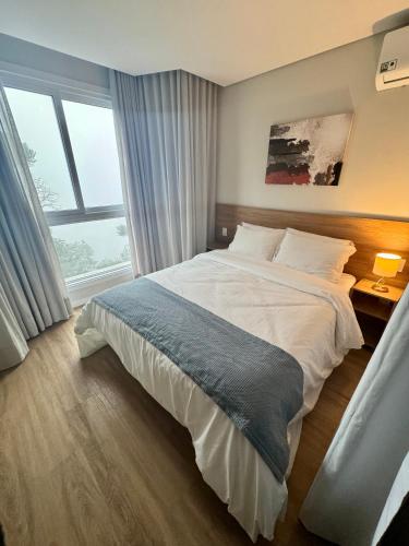 a bedroom with a large bed and a large window at Sensacional Flat Serra Class - vista do Pôr do Sol in Canela