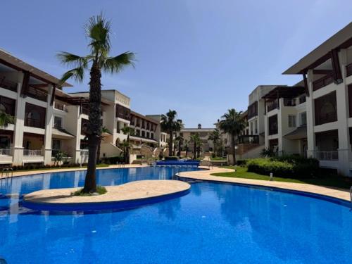 een groot blauw zwembad met een palmboom voor de gebouwen bij Front Beach - Bahia Golf Beach in Bouznika