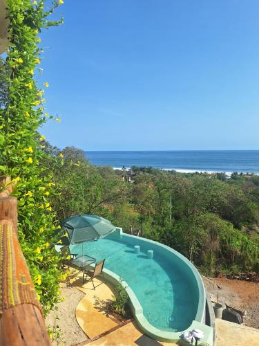 a swimming pool with an umbrella next to the ocean at Casa Jasmin Bed & Breakfast in Troncones