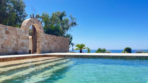 - une piscine à côté d'un mur en pierre et de l'océan dans l'établissement Auberge Ferayola, à Galéria