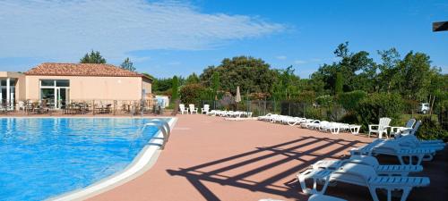 une piscine avec des chaises blanches et un bâtiment dans l'établissement Villa Résidence Les Demeures du Ventoux - Vacancéole AUBIGNAN, à Aubignan