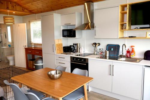 a kitchen with white cabinets and a wooden table at Cabin Cynthia in Llwyngwril