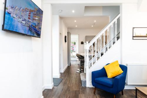 a living room with a blue chair and a staircase at Beach Haven, Steps to Sand, Trails & Shops, Highly Rated 2-Bedroom House Minutes from Mumbles Beach with a Patio in Oystermouth