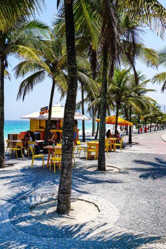 a beach with tables and chairs and palm trees at OBO Casa • Modern Lux Design Loft • Ipanema Beach in Rio de Janeiro