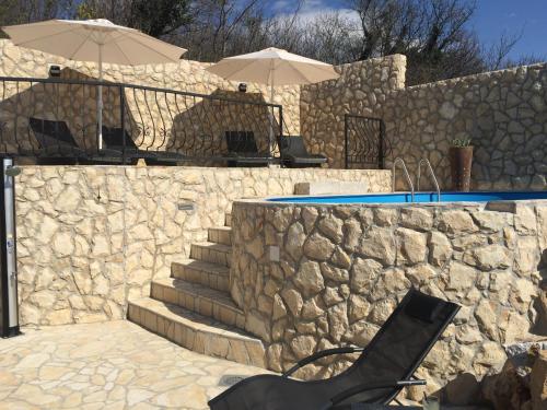 a stone wall next to a swimming pool with two umbrellas at Family friendly house with a swimming pool Bribir, Novi Vinodolski - 23474 in Bribir