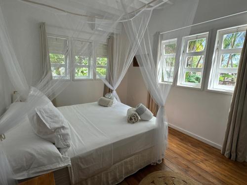 a bedroom with a bed with white sheets and windows at Le Coconut Lodge in Avatoru
