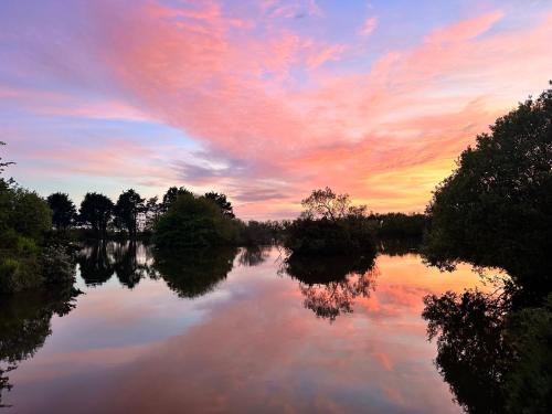 a sunset over a river with trees and clouds at Lakeside Glamping Kingfisher in Saint Columb Major