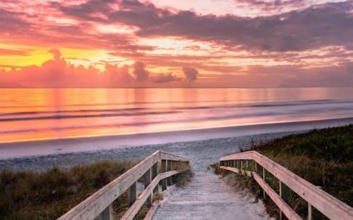 a bridge leading to the beach at sunset at Moko Hiwi Escape Ruakākā- Huia Suite in Ruakaka