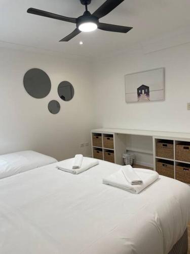 a bedroom with a white bed with a ceiling fan at Miami's Family Getaway Sleeps 10, Pool, Patio, Walk to North Burleigh Beach & Shops in Gold Coast
