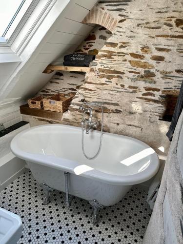 La salle de bains est pourvue d'une baignoire blanche et d'un mur en pierre. dans l'établissement Le Petit Tinténiac - T2 cosy au cœur de la Doutre, à Angers