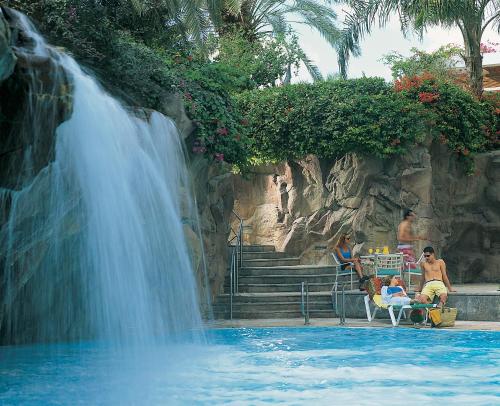 a waterfall in a pool with people sitting in chairs next to a waterfall at Royal Beach Eilat by Isrotel Exclusive in Eilat