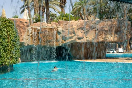 a person swimming in a pool with a waterfall at Royal Beach Eilat by Isrotel Exclusive in Eilat