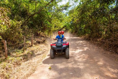two people riding on a four wheeler on a dirt road at Sunrise 6- Ocean View 2 Br Condo, Steps To The Beach in Tamarindo