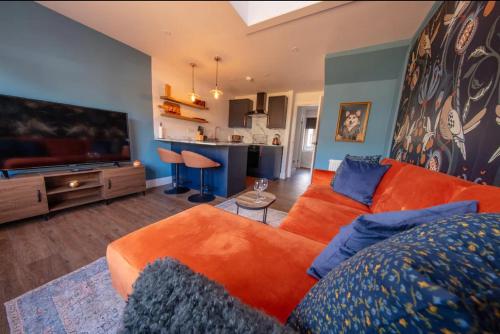a living room with an orange couch and a flat screen tv at The Bradan - Troon - Coorie Doon Stays in Troon