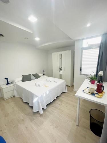 a white bedroom with a large bed and a table at AT Paseo Ficus Centenario in Almería