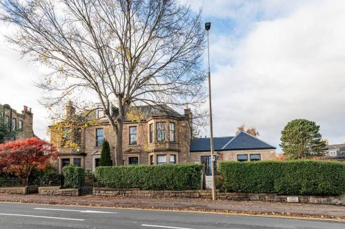 a large house with a tree in front of a street at Luxury Victorian 5 bedroom apartment by Lady road apartments in Edinburgh