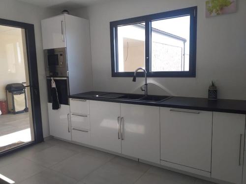 une cuisine avec des armoires blanches, un évier et une fenêtre dans l'établissement maison 3 chambres avec terrasse couverte, à Mazières-en-Mauges