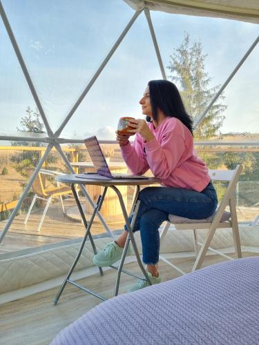 a woman sitting at a table with a laptop at Glamping 4 us in Topliţa