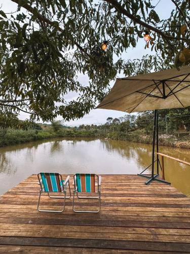 two chairs and an umbrella on a dock next to a river at Hospedagem Ônibus na Roça em Serra ES in Serra