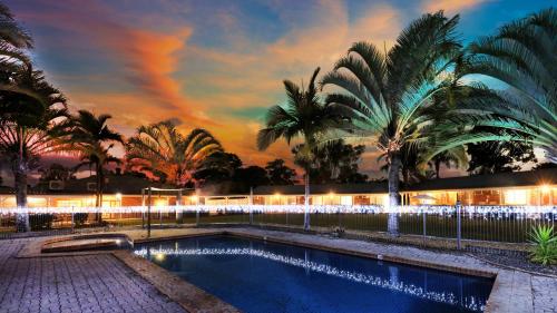 a pool with palm trees in front of a building at Koorawatha Homestead Motel in Bororen