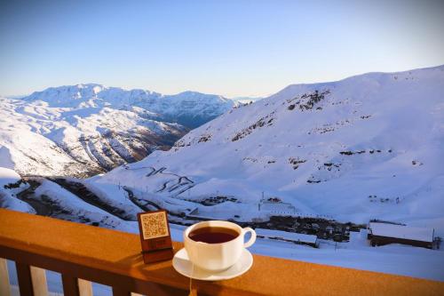 a cup of coffee sitting on a table with a snow covered mountain at HOM I Edificio Valle Blanco Valle Nevado 2D2B SKI IN&OUT in Farellones