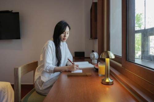 a woman sitting at a table writing on a piece of paper at Surim Hotel Sokcho by AanK in Sokcho