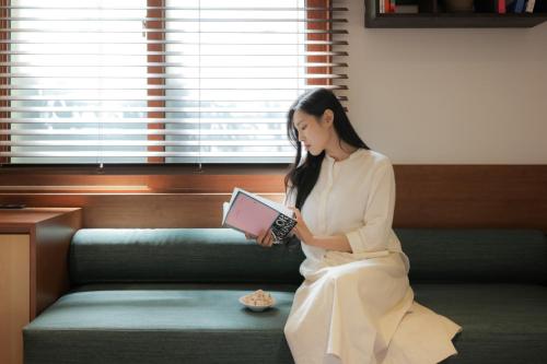 a woman sitting on a couch reading a book at Surim Hotel Sokcho by AanK in Sokcho