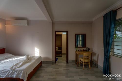 a bedroom with a bed and a desk and a table at Coconut Lodge in Kampot