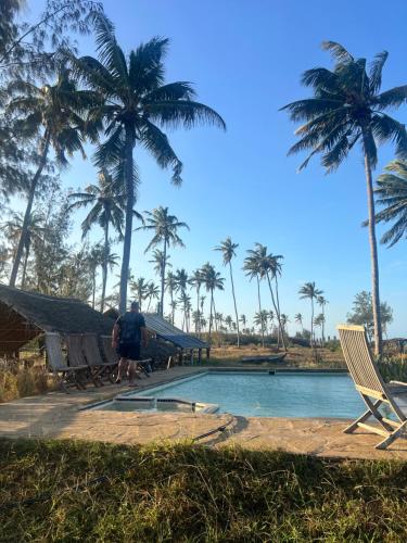 a man standing next to a swimming pool with palm trees at Chuiba Palms in Pemba