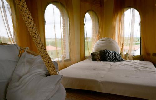 a bedroom with a bed with white sheets and windows at Palazzo delle Biscie - Old Tower & Village in Molinella