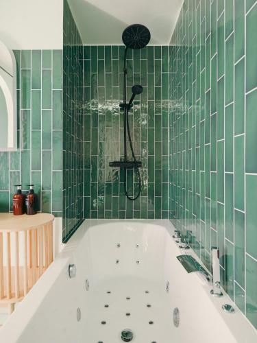 La salle de bains carrelée de vert est pourvue d'une baignoire blanche. dans l'établissement Alcova - Stade de France - Jacuzzi - Cinema, à Saint-Denis