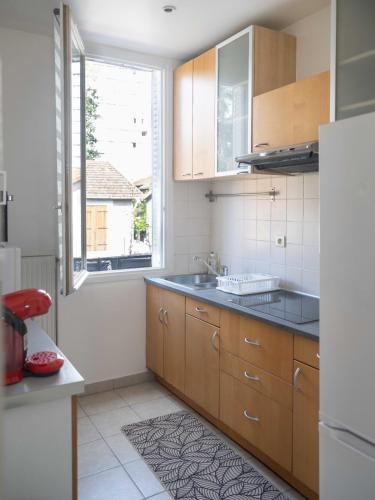 une cuisine avec des armoires en bois, un évier et une fenêtre dans l'établissement Le Cocon Raffiné, à Bagneux