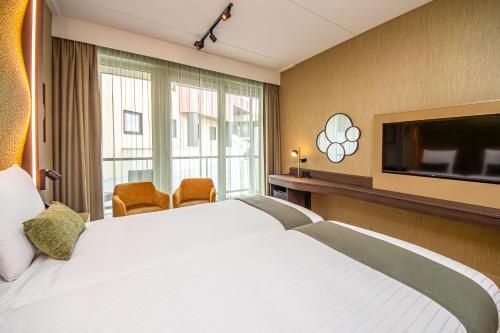 a hotel room with a large bed and a flat screen tv at Strandhotel Het Hoge Duin in Wijk aan Zee