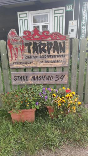 a sign for a farm with flowers in front of a house at KTA TARPAN Podlaski Dom in Narewka