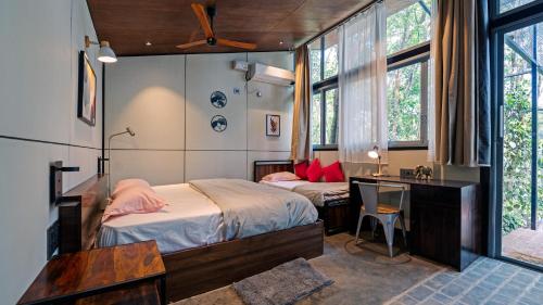 a bedroom with two beds and a desk and windows at Cove by Raho in Siddapur