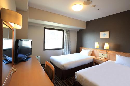 a hotel room with two beds and a flat screen tv at Smile Hotel Tokushima in Tokushima