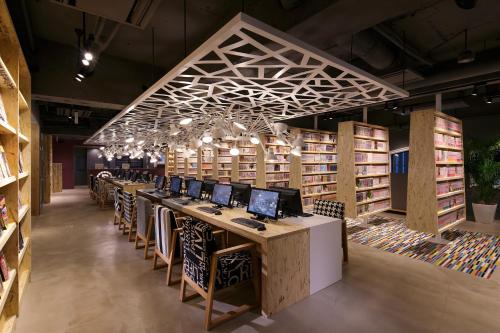 una biblioteca con una mesa larga con ordenadores. en Booth Netcafe & Capsule, en Tokio