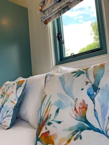 a couch with two pillows and a window at St. Kew Shepherd Huts in Wadebridge