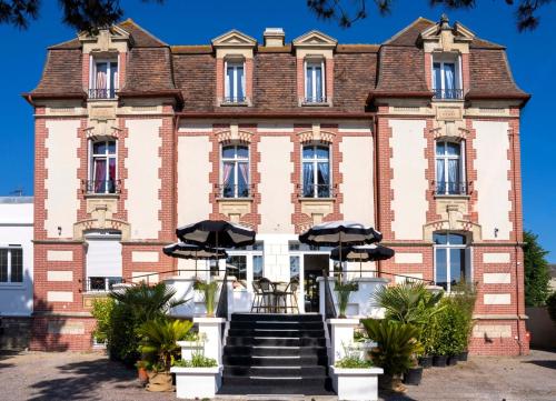 an old brick building with umbrellas in front of it at Villa Victoria Hôtel et Spa in Ouistreham